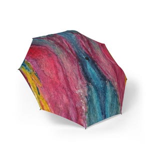 Pode incluir: Um guarda-chuva aberto com um design abstrato vibrante. A cobertura do guarda-chuva apresenta uma mistura de cores, incluindo rosa, azul, amarelo e vermelho, criando um efeito de aquarela. O design tem uma aparência texturizada.