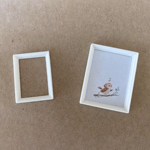 Peut inclure: Deux cadres photo blancs sur un fond brun. Le plus grand cadre contient une image d'un oiseau brun chantant sur une branche. Le plus petit cadre est vide.