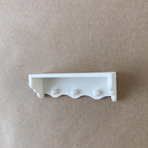 Può includere: Mensola in legno bianco con bordo a festoni e tre pomelli rotondi. La mensola è progettata per il montaggio a parete.