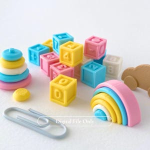 May include: A collection of colorful toy blocks, a rainbow stacker, and a paperclip. The blocks are in various colors, including yellow, pink, and blue, with numbers on them. A wooden car is also visible. The image has the text "Digital File Only".