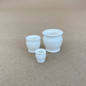 Puede incluir: Tres macetas de cerámica blanca de diferentes tamaños. Las macetas son redondas y tienen un borde ligeramente acampanado.