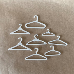 May include: Seven white plastic hangers of varying sizes. The hangers are arranged in a semi-circle on a brown surface.