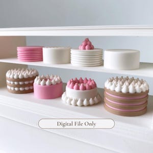 Può includere: Una collezione di modelli di torte in miniatura esposti su un supporto bianco a più livelli. Le torte presentano vari design, tra cui strati a righe rosa e bianche, superfici bianche lisce e dettagli di glassa. Il testo Digital File Only è visibile.
