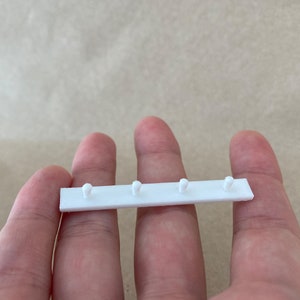 Może przedstawiać: Biały pasek z tworzywa sztucznego z pięcioma małymi, okrągłymi gałkami, prawdopodobnie służący do zawieszania przedmiotów.