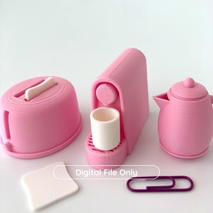 以下が含まれることがあります： ピンク色のミニチュアキッチンセット。トースター、白いカップ付きコーヒーメーカー、ティーポットが含まれています。白い正方形と紫色のペーパークリップも存在します。「Digital File Only」のテキストが表示されています。