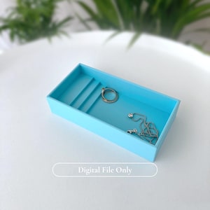 Puede incluir: Una bandeja rectangular de joyería azul claro con un interior escalonado. Dentro de la bandeja hay un collar de plata con un pequeño colgante y un anillo. El texto "Digital File Only" está en la parte inferior.