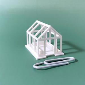 Könnte beinhalten: Ein weißes Plastikmodell eines Gewächshauses mit einfachem Design. Das Modell ist klein, etwa so groß wie eine Büroklammer.
