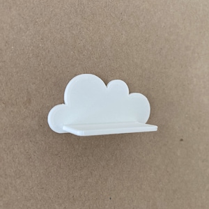 Könnte beinhalten: Weißes, wolkförmiges Wandregal mit einer ebenen Fläche. Das Regal ist aus Kunststoff und zum Anbringen an einer Wand konzipiert.