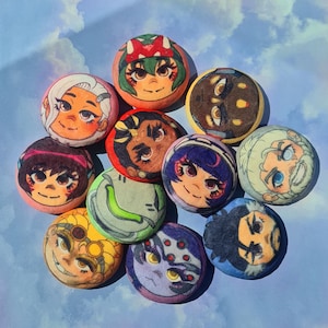 May include: A collection of round, colorful buttons featuring various cartoon character portraits. The buttons showcase a variety of skin tones, hair colors, and facial expressions. The background is a light blue with a cloudy pattern.