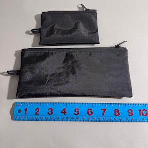 May include: Two black zippered pouches of different sizes. The larger pouch is approximately 9 inches long, and the smaller pouch is about 4 inches long. Both pouches have a shiny, textured appearance and a small loop on one end.