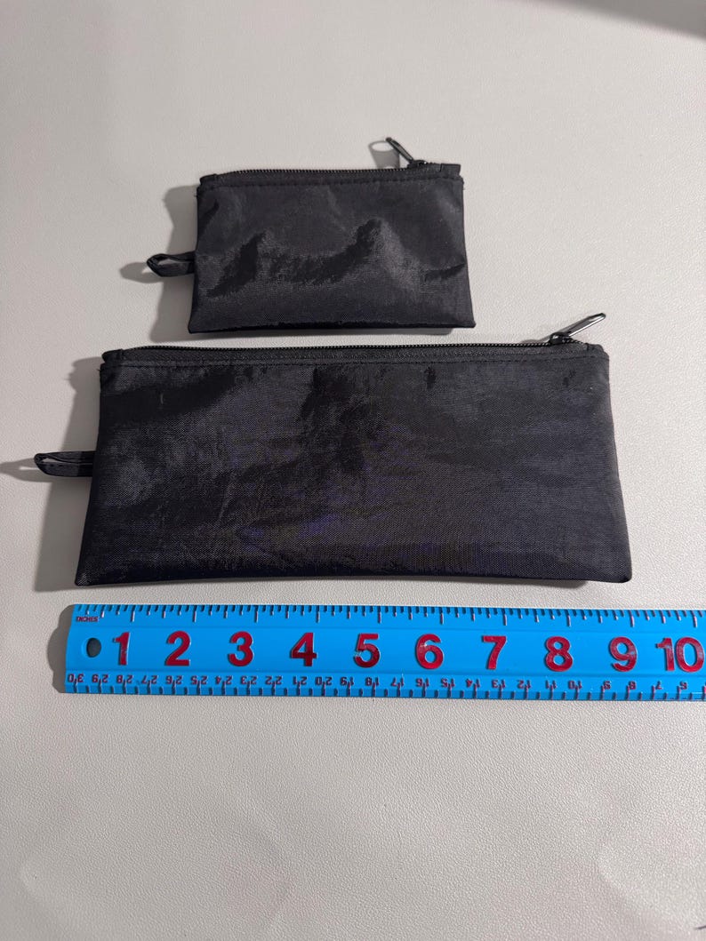 May include: Two black zippered pouches of different sizes. The larger pouch is approximately 9 inches long, and the smaller pouch is about 4 inches long. Both pouches have a shiny, textured appearance and a small loop on one end.