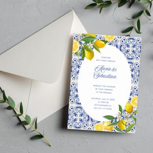 Puede incluir: Una tarjeta de invitación de boda rectangular con un centro ovalado blanco que presenta texto azul y un borde con patrón de azulejos azul y blanco decorado con limones amarillos y hojas verdes, junto a un sobre blanco a juego.