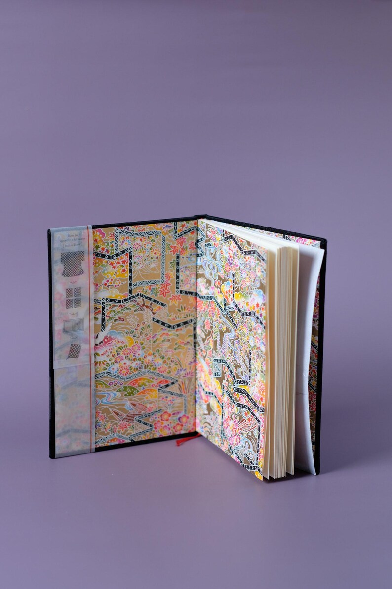 May include: An open black journal with a colorful patterned cover. The pages are blank and the journal is open to the middle.