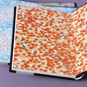 May include: Three notebooks with different patterned covers. The first cover has a colorful floral design, the second has a blue and white floral design, and the third has a red and white floral design.