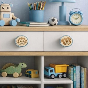 May include: A white and wood-toned children's bookcase with three drawers and open shelves. The drawers have bear and monkey-themed knobs. The shelves hold toys, books, and storage bins. A blue and white star-patterned bed is visible.