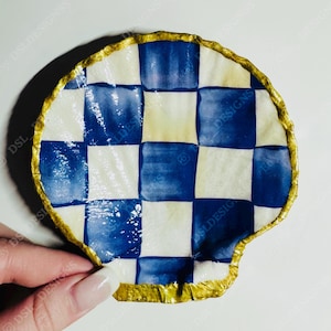 May include: A decorative, hand-painted seashell-shaped dish. The dish has a blue and white checkered pattern with a gold trim. A unique piece of home decor, it measures approximately 10 cm in diameter.