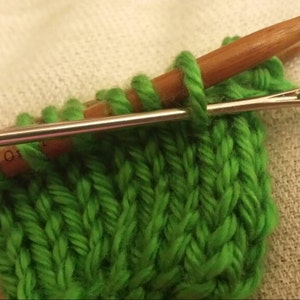 Może przedstawiać: Zbliżenie na zielony dzianinowy materiał z drewnianym drutem do robótek na drutach i metalowym drutem do robótek na drutach. Metalowy drut jest nawleczony zieloną nicią.