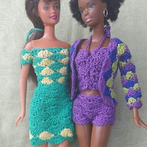 May include: Two dolls wearing crocheted outfits. One doll is wearing a green and yellow dress, the other is wearing a purple and blue top and shorts.