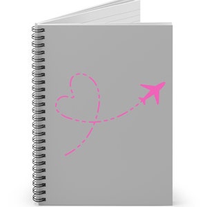 May include: A spiral-bound notebook with a gray cover. A pink airplane graphic flies through a heart-shaped dotted line. The notebook's pages are white and lined.