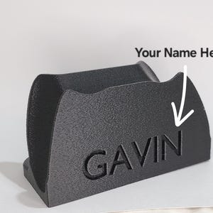Può includere: Un organizzatore da scrivania nero personalizzato con il nome "GAVIN" inciso sul davanti. L'organizzatore ha una superficie testurizzata e un design curvo.