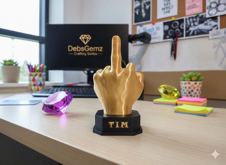 Pu&ograve; includere: Una scultura a forma di mano color oro che mostra il dito medio, montata su una base nera con il nome "TIM" in lettere dorate. La scultura &egrave; su una scrivania con un computer e forniture per ufficio.