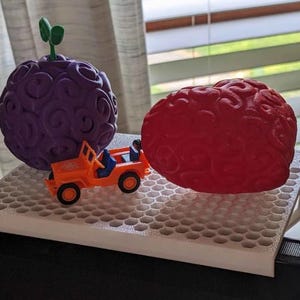 Może przedstawiać: Zabawkowy jeep pcha fioletowy i czerwony przedmiot w kształcie m&oacute;zgu na białej platformie z wzorem plastra miodu.