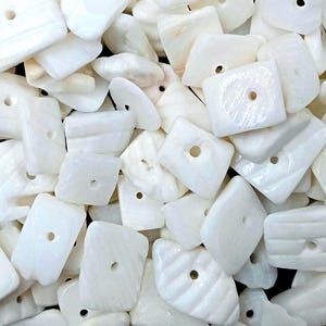 May include: A collection of white shell beads with irregular geometric shapes. Each bead features a smooth, pearlescent surface and a single centered hole for threading. The pieces vary in size and form, displaying natural textures and variations.