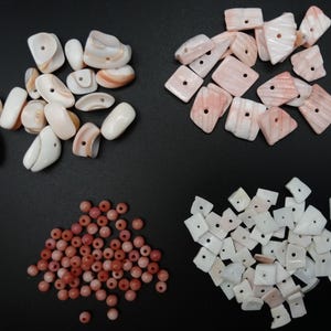 May include: A collection of jewelry making components including white and peach-colored curved shell beads, flat rectangular pink-striped shell pieces, small round reddish-pink stone beads, and small irregular white shell fragments with holes.