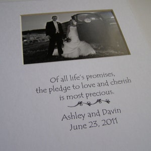 May include: Black and white wedding photo of a couple standing in front of a car. The photo is framed with a white mat and has the text "Of all life's promises, the pledge to love and cherish is most precious. Ashley and Davin June 23, 2011" printed below it.