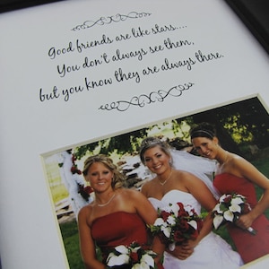 May include: Framed photo with a white mat and black frame. The photo features three women, one in a white wedding dress and two in red dresses, holding bouquets. Above the photo is the text: "Good friends are like stars... You don't always see them, but you know they are always there."