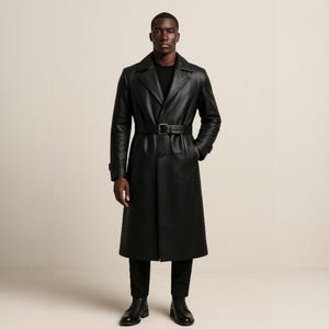 May include: A full-length black leather trench coat with a belt cinching the waist. The coat has a classic lapel and is worn with black pants and shoes. The model is standing in front of a neutral background.