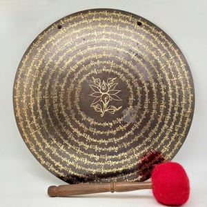 May include: A large, round, bronze gong with intricate gold lettering and a central flower design. It comes with a wooden mallet with a red felt head.