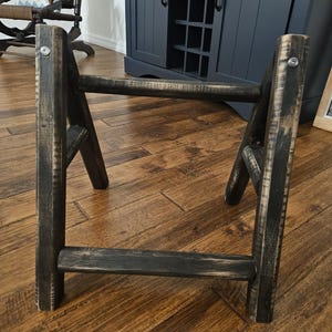 May include: A black wooden A-frame stand with two shelves. The stand is made of distressed wood and has a rustic look.