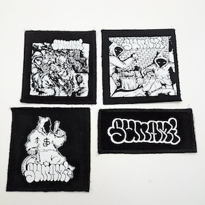 May include: Four black and white iron-on patches with the word "Surreal" in a graffiti style font. The patches feature different designs, including a hooded figure, a group of figures, and a single figure with a gun.