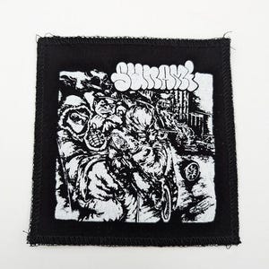 May include: Square black patch with a white graphic illustration and the word "SURVIVE" in a stylized font. The illustration depicts a chaotic scene with figures and vehicles.