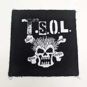 May include: Black square patch featuring the text "T.S.O.L." in white block letters above a white skull with spiky hair and crossed bones. The names "Jack", "Mike", "Ron", and "Todd" are written on the bones.