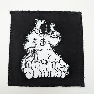 May include: Black square patch with a white graphic of a hooded figure holding two guns. The figure has a dollar sign on the chest. The word "SHRAKS" is written in white graffiti-style lettering below the figure.