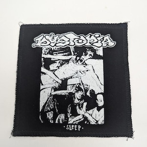 May include: Black square patch with a white graphic of a band logo and artwork. The word "DYSTOPIA" is in a stylized font above a detailed black and white illustration. The word "SLEEP" is below the illustration.