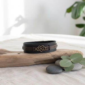 Puede incluir: Una pulsera de cuero negro y marr&oacute;n con un dije de coraz&oacute;n infinito de color bronce. La pulsera de pu&ntilde;o se exhibe sobre madera flotante, sobre un fondo neutro. La pulsera es de estilo pu&ntilde;o.