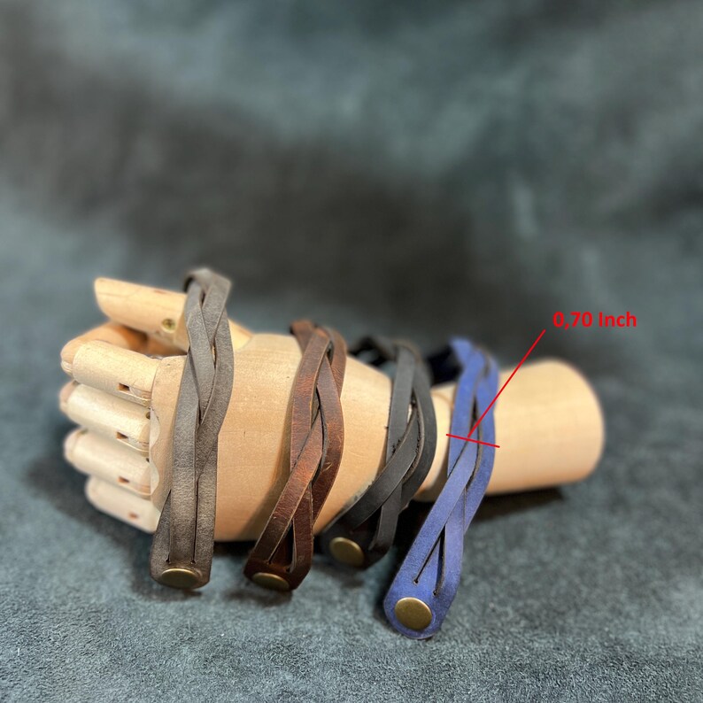 May include: Four braided leather bracelets in gray, brown, black, and blue. Each bracelet features a metallic snap button closure and a width of 0.70 inches as indicated by the red text and line pointing to the blue bracelet's strap.