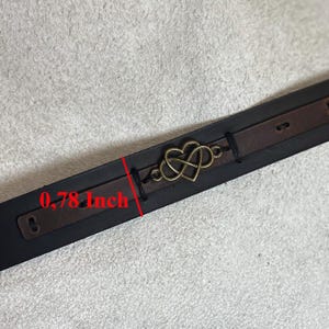 Puede incluir: Una pulsera de cuero con un dije de coraz&oacute;n y s&iacute;mbolo de infinito de color bronce. La pulsera es negra con una correa de cuero marr&oacute;n y mide 2 cm de ancho.