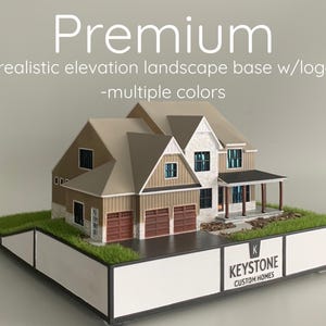 May include: A detailed architectural model of a house with a realistic landscape base. The model features multiple colors, including brown, beige, and white, with a garage and a porch. The base includes the "KEYSTONE CUSTOM HOMES" logo.