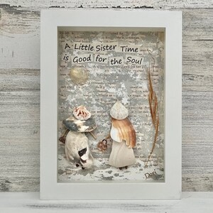 May include: A framed artwork featuring a gray background with a white text overlay that reads "A Little Sister Time is Good for the Soul". The artwork is decorated with seashells and a piece of dried grass.