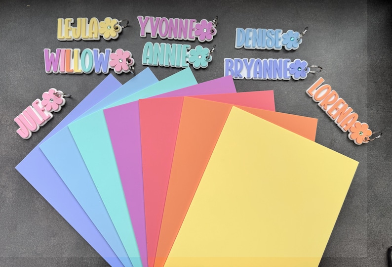 May include: A collection of colorful name tags with flower accents and a variety of pastel-colored paper sheets. The name tags include names like Lejla, Yvonne, Denise, Willow, Annie, Bryanne, Jules, and Lorena.