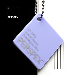 May include: A square, light purple Perspex color swatch with the text "SA 7490 Sweet Pastels Bubblegum Blue" and the brand name "PERSPEX" in silver. The swatch is attached to a silver ball chain.