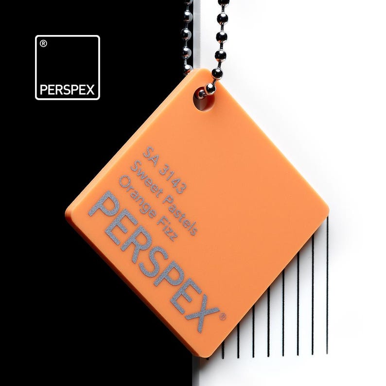 May include: An orange Perspex color swatch, square-shaped, hanging from a silver ball chain. The swatch has the text "SA 3143 Sweet Pastels Orange Fizz" and the brand name "PERSPEX" in silver. The background is black and white.