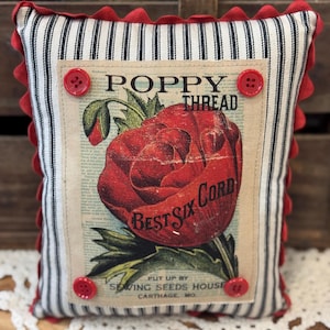 Może przedstawiać: Kwadratowa poduszka dekoracyjna z czarno-białym wzorem w paski i czerwonym wykończeniem. Na środku znajduje się nadruk w stylu vintage z czerwoną makiem z napisem "POPPY THREAD BEST SIX CORD". Czerwone guziki są wszyte w każdym rogu.