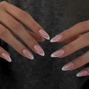 May include: Close-up of hands with long, almond-shaped nails. The nails are painted with a light pink base and a white French tip. The nails are glossy and well-manicured, showcasing a classic nail design.