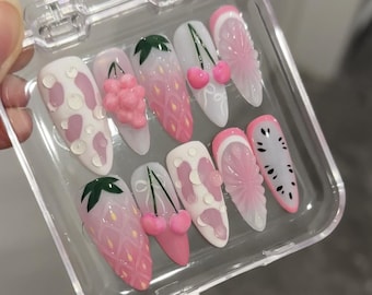 May include: A set of ten pink and white false nails with different fruit designs. The designs include cherries, strawberries, watermelon, and grapes.