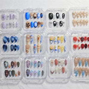 May include: A set of 10 clear plastic containers, each containing 10 false nails with different designs. The designs include stars, flowers, seashells, and abstract patterns. The nails are in various colors, including white, blue, red, and yellow.